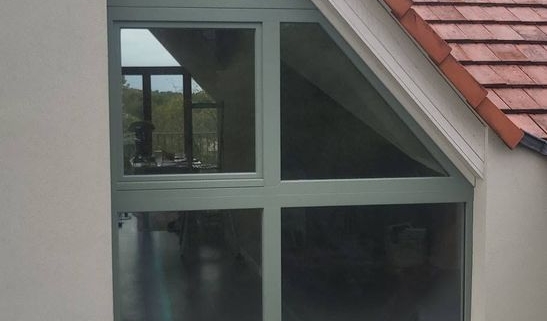 Ensemble de fenêtres en mélèze triple vitrage sous un pignon triangulaire, vue extérieure