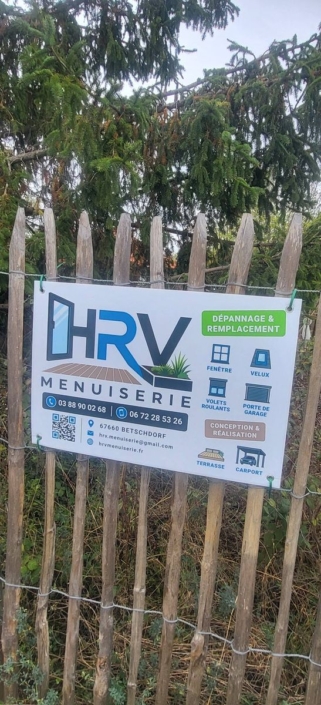 Panneau de chantier HRV Menuiserie sur une clôture