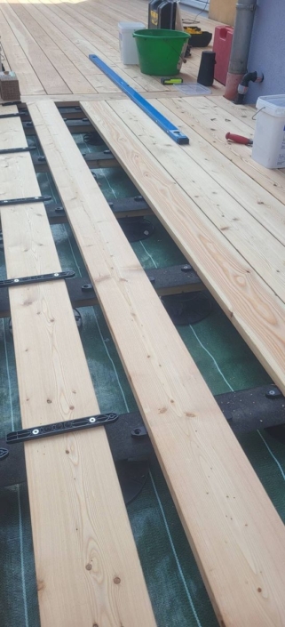 réalisation d’une terrasse en mélèze du Canada avec fixation invisible Pose des lames de mélèze sur lambourdes avec clips de fixation invisible et toile géotextile