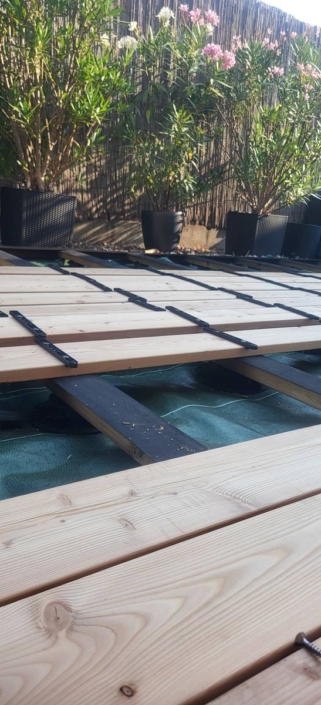 réalisation d’une terrasse en mélèze du Canada avec fixation invisible Détail des clips noirs de fixation invisible entre les lames de la terrasse en mélèze